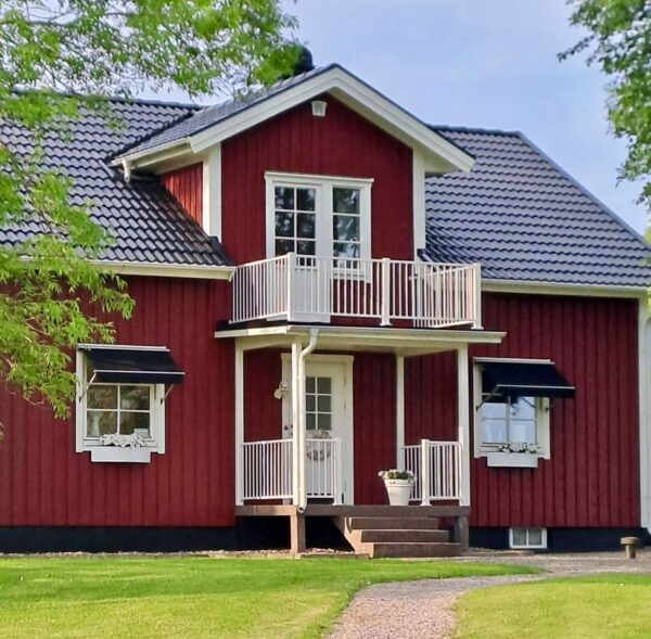 Lantligt falurött hus med vita knutar. Vitt underhållsfritt staket vid entré och på balkong.