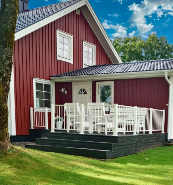 Uteplats i en lantlig miljö. Vitt staket till en faluröd villa.