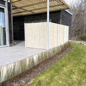 Avskärmning till utekök på en uteplats med betong och klinker. Stående staket som en ribbvägg som ger en modern och stilren känsla.